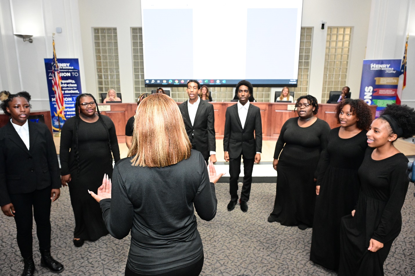 A group of people in black dresses standing in front of a screenDescription automatically generated